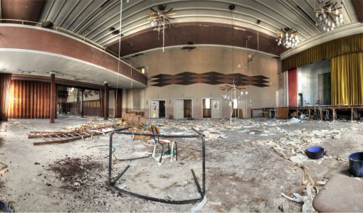 Verlassener Saal mit Bühne und Balkon.